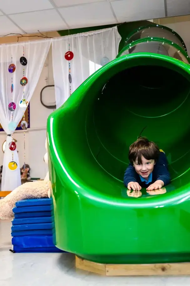 boy in nursery sliding down a green slide